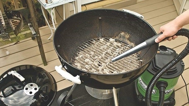 a hand vacuuming a charcoal kettle barbecue