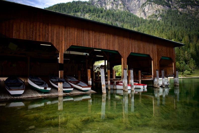 log cabin boat store with boats moored in green waters at the foot of a mountain