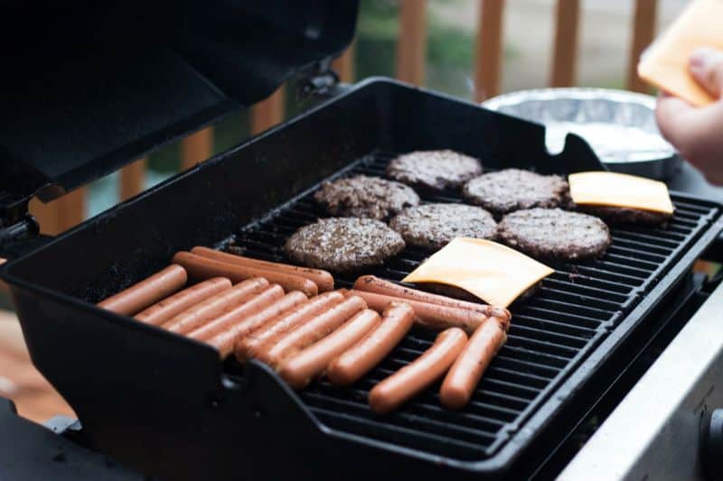 burgers, sliced cheese, and sausages cooking on BBQ