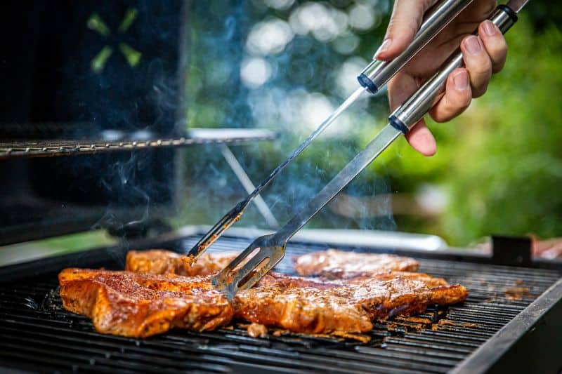 steaks being pressed into BBQ grill with tongs