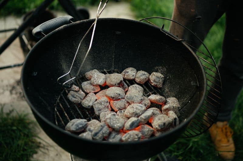 kettle charcoal bbq filled with white hot coals and someone tending them with tongs